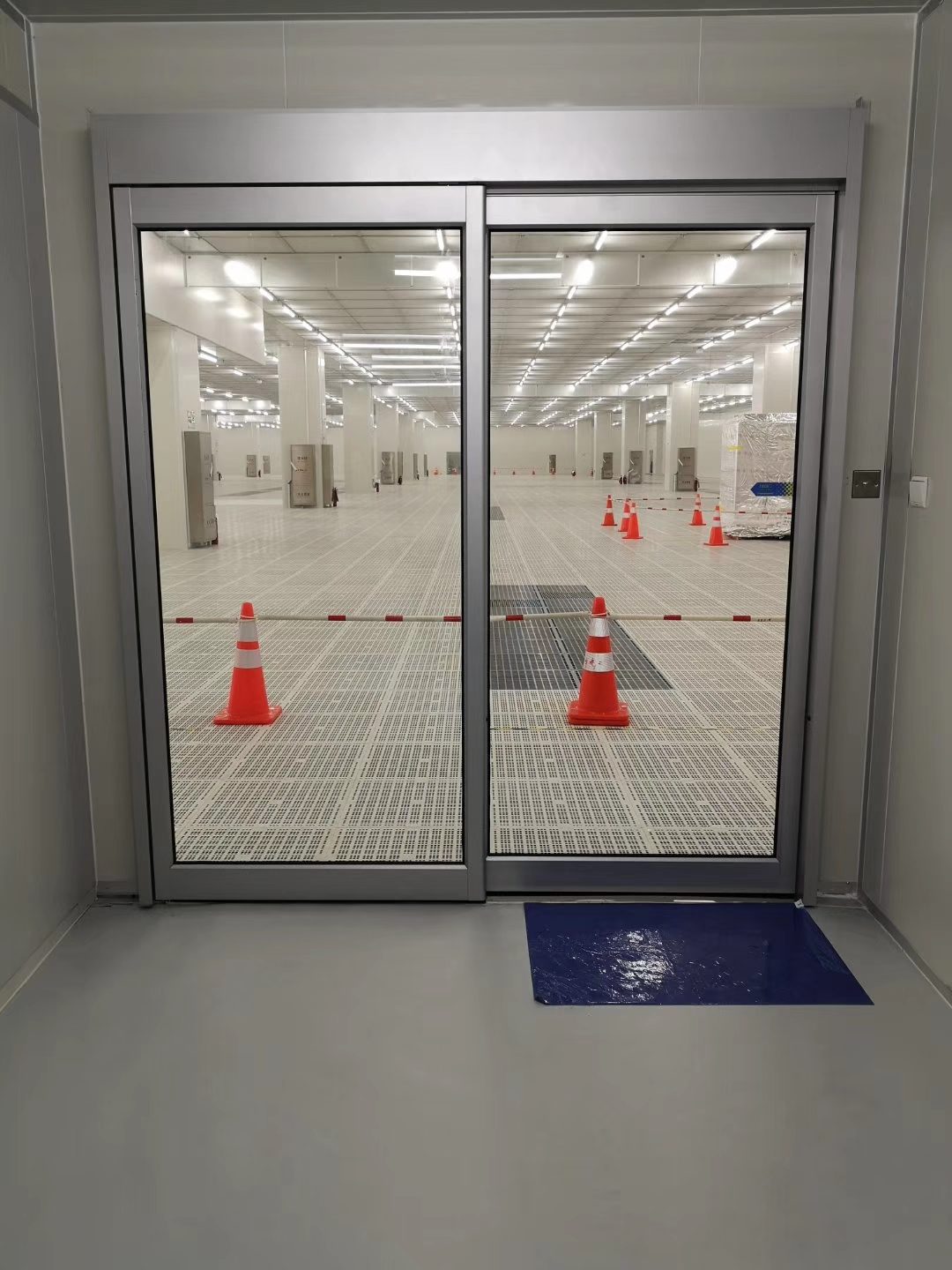 洁净区自动门:双扇玻璃门,室内平整地面,门口设警示锥与地垫