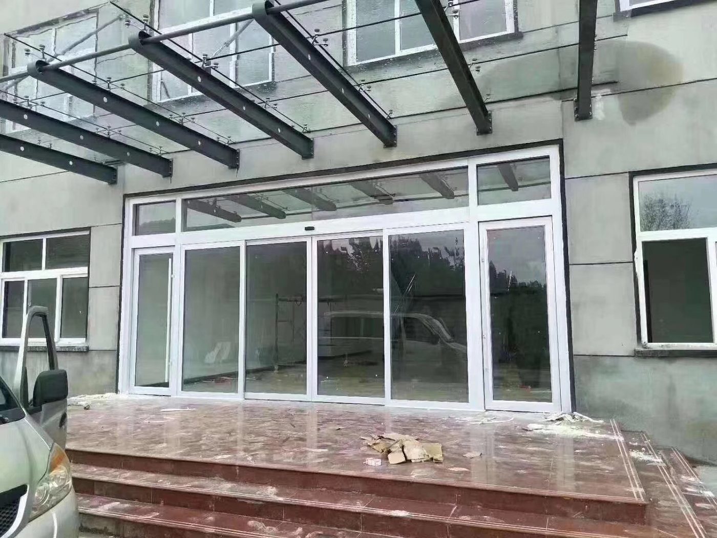 室外雨棚自动门：雨棚下的玻璃自动门，门前为红色石材台