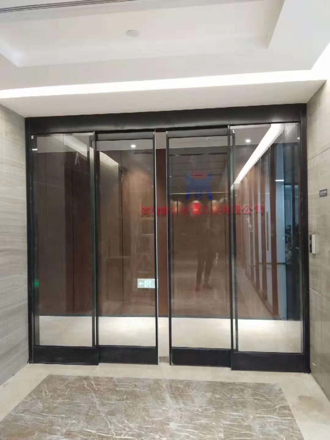 商厦自动门：商场内部的双扇玻璃自动门，深色门框与红毯地面